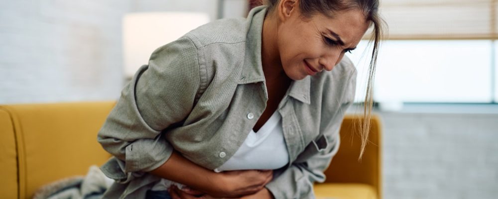 Young woman suffering from stomach cramps sitting on the sofa.